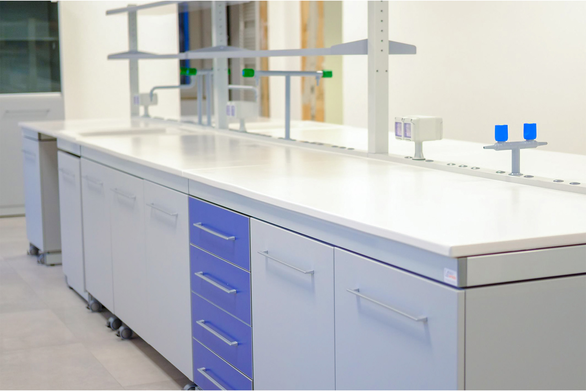 Laboratorio controllo qualità con banchi tecnici blu, piano gres monolitico e postazioni ergonomiche